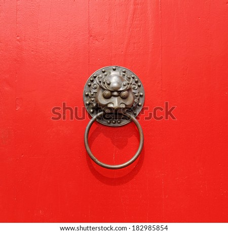 A medieval, oriental gargoyle head brass door knocker on a red wooden door panel.