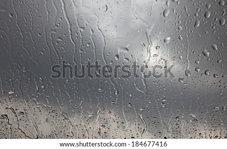 Rain droplets on a window glass pane with dark stormy clouds in the background.