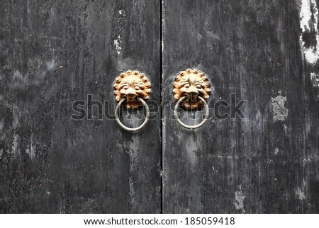 A pair of vintage medieval gargoyle head door ring on an ashen wooden door panel.