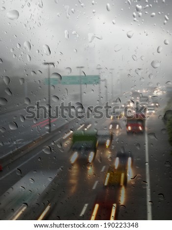 Rain droplets on a window glass pane with view of light trails of motor vehicle traveling on a wet and slippery highway after a heavy rainstorm.