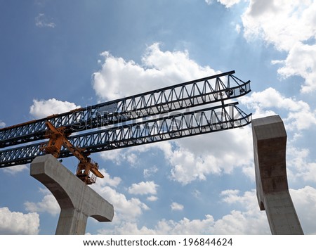 An elevated highway gantry crane with an extender mechanical guide at a construction site against a blue cloudy sky.