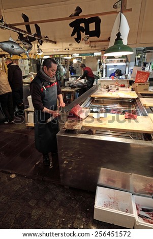 TOKYO - DECEMBER 24, 2014: A fishmonger cuts a tuna block at his booth in the Tsukiji Fish Market in Tokyo, Japan. The Tsukiji fish market is the biggest wholesale seafood market in the world.