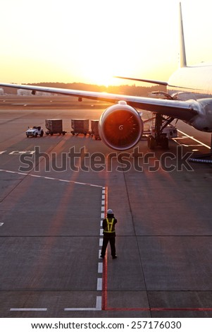 A airport traffic controller ground crew guiding an airplane on an airport runway against a fiery sunset.