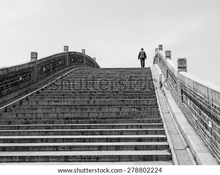 Silhouette of a man walking across an ancient Chinese imperial stonemason bridge, processed in monochrome.