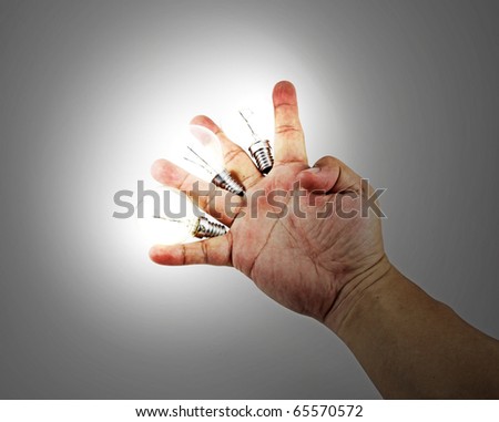 An isolated hand holding three lighted incandescent light bulb between the fingers which illuminate the area.