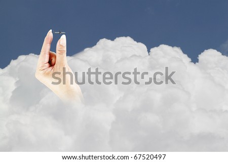 An image of a female hand reaching out of a large cumulus cloud to guide an airplane to safety over inclement weather.