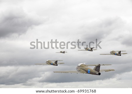 A squadron of military air force fighter jet flying in a battle attack formation over a cloudy overcast sky.