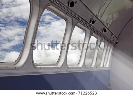 A surrealistic image of sunshine beam illuminating an airplane cabin through its window as it flies through a blue cloudy sky.