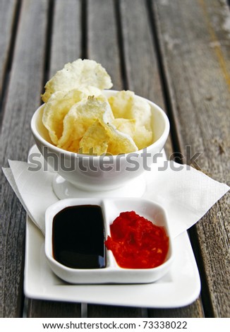 A bowl of crunchy tapioca cracker served together with its condiment of soy sauce and chili paste.