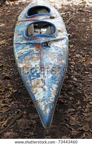 A colorful weathered kayak also known as a canoe resting on a dirty dried river bed.
