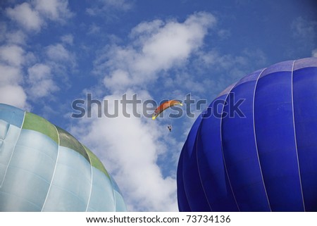 A paraglider making a risky move to fly between two hot air balloons during a hot air balloon festival.