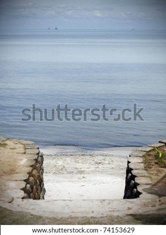 Stone stairway passage to a serene calm beach facing a blue sea.