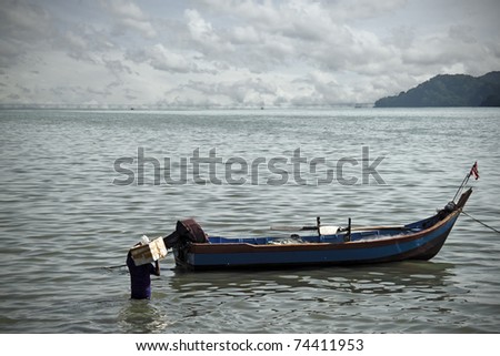 Rural timber sampan boat with outboard motor being loaded with goods for transportation to rural coastal village.