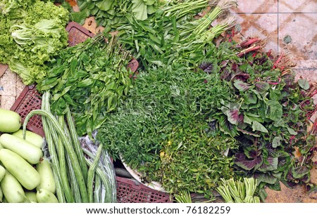 Fresh green leafy vegetables and melon displayed on the floor of an Asian wet market.