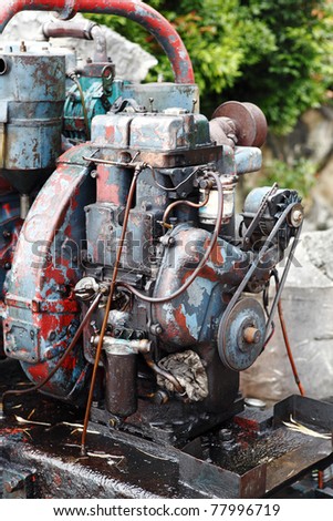 A colorful dilpidated old greasy water pump engine in a rural forest surrounding.