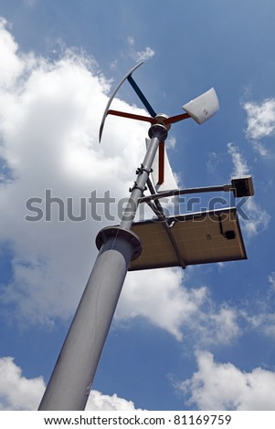 A multi energy generating street light device using sustainable solar power and wind energy via a wind turbine, against a blue cloudy sky.