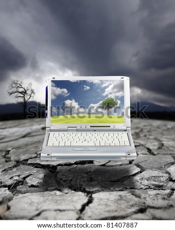 A modern computer laptop showing a tree growing on a fertile green field with cloudy blue sky on its screen, in contrast to a drought stricken arid landscape with a dying tree due to global warming.