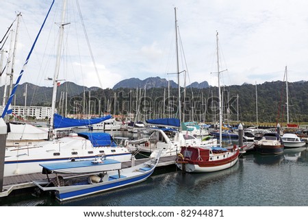 Sailboat and yacht docked at a coastal marina in Langkawi Island, Malaysia, overlooking  green hills against a dramatic morning sky.
