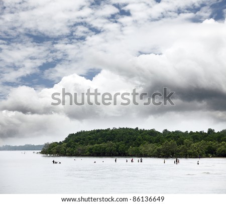 An unidentified crowd of people having fun by the sea in Port Dickson, Malaysia against a surreal dramatic cloudy sky.