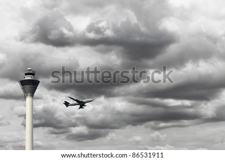 An airplane taking off during a stormy cloudy day overlooking the airport control tower.
