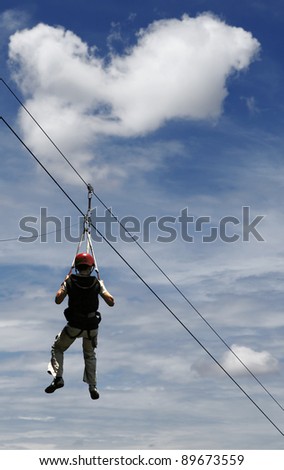 A man gliding on the flying fox contraption against a blue cloudy sky.