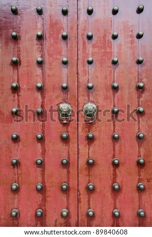 Surface of a brown rustic vintage oriental solid timber door with ornamental brass stud and traditional dragon knocker.