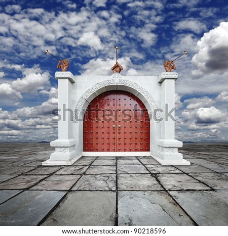 Musician trumpeter blowing its horn to welcome guest at a vintage palace gate with solid timber rustic doors with brass studs against a blue cloudy sky.