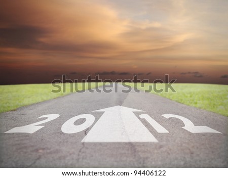 White print of year 2012 and a forward arrow on an old tarmac road vanishing into the horizon of a surreal fiery sunset, for the concept of a cataclysmic future for year 2012.