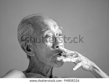 An old wrinkly emaciated Chinese man smoking a cigarette in monochrome.