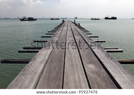 An old grungy timber jetty extending into the sea with passing ships, on the Tan Jetty, which is a UNESCO heritage site, in Penang, Malaysia.