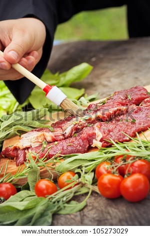Cooking ingredients: marinated meat,oil,vinegar, herbs and vegetables. Chef is carving and marinating meat.