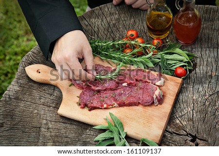 Cooking ingredients: marinated meat,oil,vinegar, herbs and vegetables. Chef is carving and marinating meat.