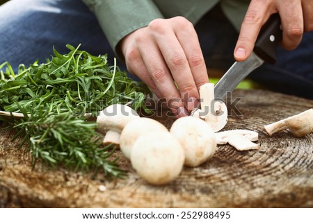 Cook is preparing food. Cutting mushrooms on wood board