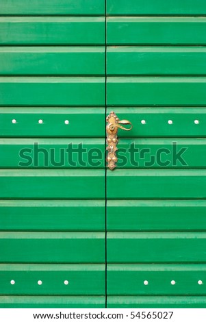 Ornate brass door handle on the green wooden door.