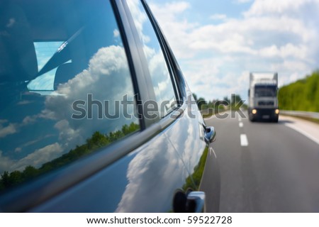 View through the rear mirror on the approaching truck on the highway. Beautiful reflections of the clouds in the windows. Shallow depth of field.