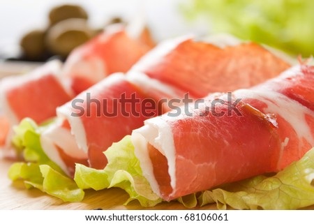 Slices of prosciutto rolled up and arranged on a lettuce leaf. Shallow depth of field.