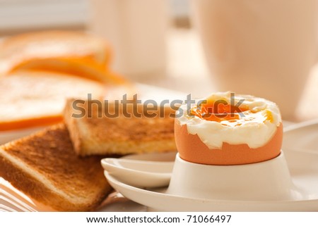Soft boiled egg with toasted bread and slices of oranges in the back. Shallow depth of filed.
