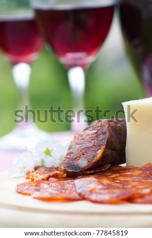 Two glasses of red wine with sausage and cheese on a picnic table