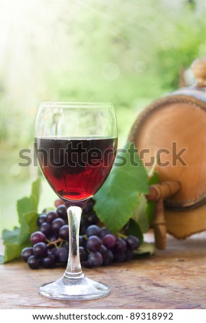 Glass of red wine with fresh harvested grapes and wine barrel
