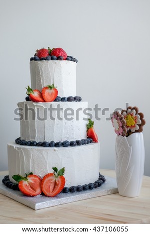 side view on big white cake decorated with red strawberry and black berry