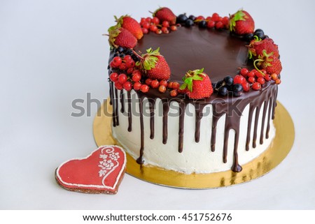 view from top birthday cake decorated by chocolate and berry, strawberry on top near red gingerbread like heart shape on white background
