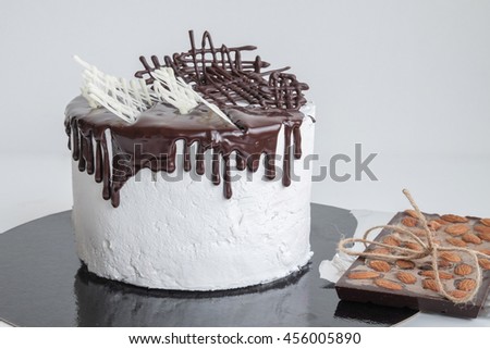 sweet cake for any celebration drizzled top with chocolate and abstract decorated near lay chocolate bar with nuts on foil on white background