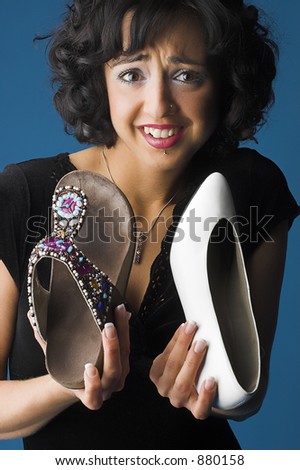 Female Brunette model holding pair of shoes and looking confused