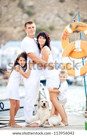 Happy young family in white clothing have fun and play with beautiful dog at vacations  on berth in summer
