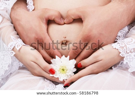 Male and female hands forming heart over belly. Female hands hold a white flower in the bottom of 