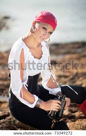 Beautiful sexy woman wearing pirate costume with field-glass at the sea coast