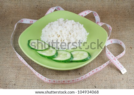 diet food. A handful of rice and cucumbers on the green plate on a rough burlap cloth