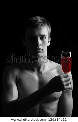 Young man with naked torso with a glass of red wine on a black background. low key