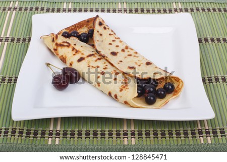 Pancake with black currants on a square plate. Bamboo green tablecloth