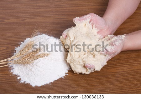 Baker\'s hands in the dough, wheat white flour and wheat ears on the wooden table